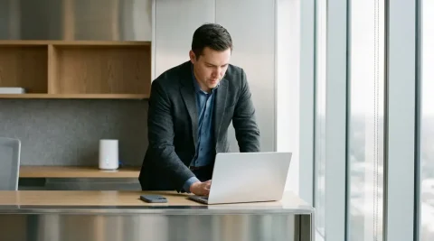 Professional werkt op laptop aan modern bureau met WiFi 6 router op de achtergrond in kantooromgeving.