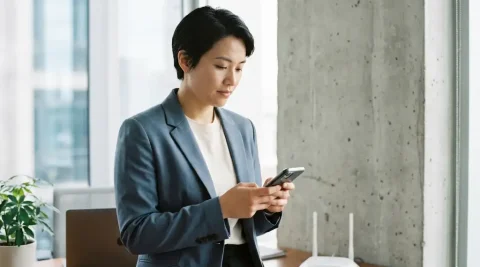 Professional houdt smartphone vast naast draadloze router op bureau, met dikke betonnen muur die wifi-signaalsterkte beïnvloedt.