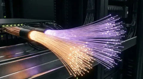 Glasvezelkabel splitst in amber en violet lichtstromen in donkere serverruimte, met metalen kabelgoten op de achtergrond.