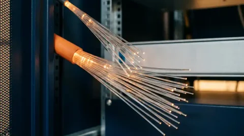 Oranje glasvezelkabel die opsplitst in meerdere dunne glasvezels in een professionele netwerkkast, met zichtbare lichtpulsen.