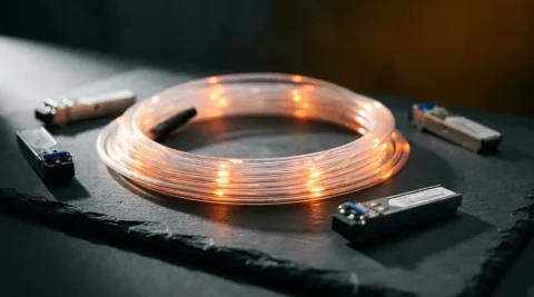 Glasvezelkabel met oranje lichtpulsen op leisteen oppervlak, omringd door SFP-transceivers, macro-opname met dramatische belichting.