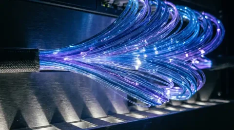 Bundel glasvezelkabels met blauw en violet licht op een donker serverrek, kwantuminspiratie zichtbaar in de lichtsporen.