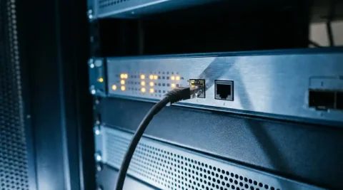 Netwerkswitch met knipperende amber waarschuwingslichten in serverrack, losse ethernetkabel naast lege poort.