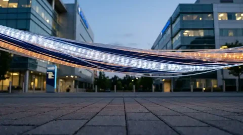 Gloeiende glasvezelkabel verbindt twee moderne ziekenhuisgebouwen bij schemering, met zachte lichtpulsen in klinisch wit en marineblauw.